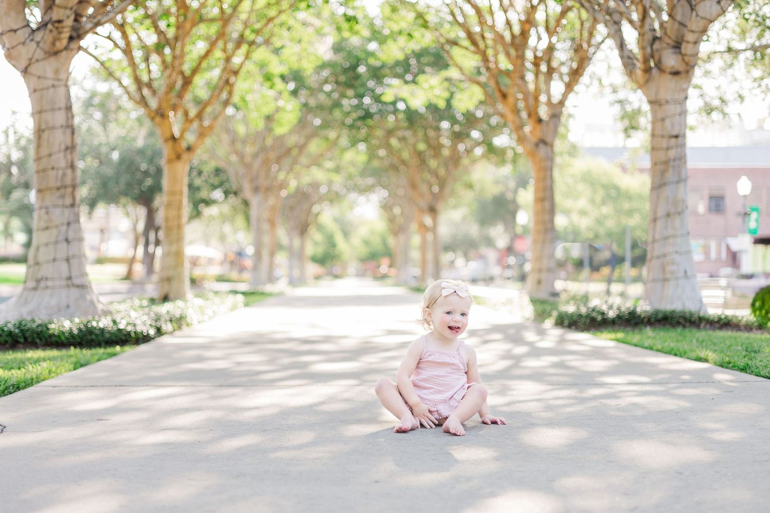 Child in pink outfit plays on tree-lined pathway during sunny day.