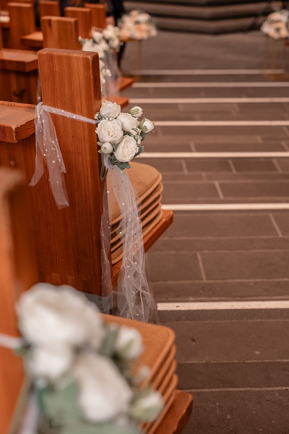 White tulle and floral decorations adorn wooden church pews for a wedding ceremony.