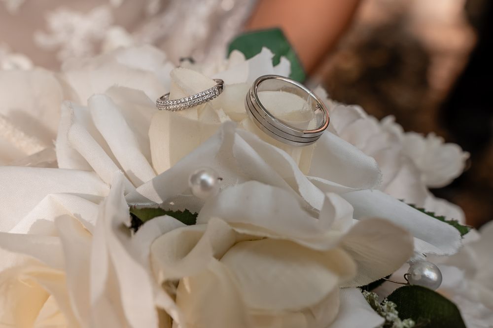 Wedding rings rest delicately on white rose petals in an elegant bridal detail shot.
