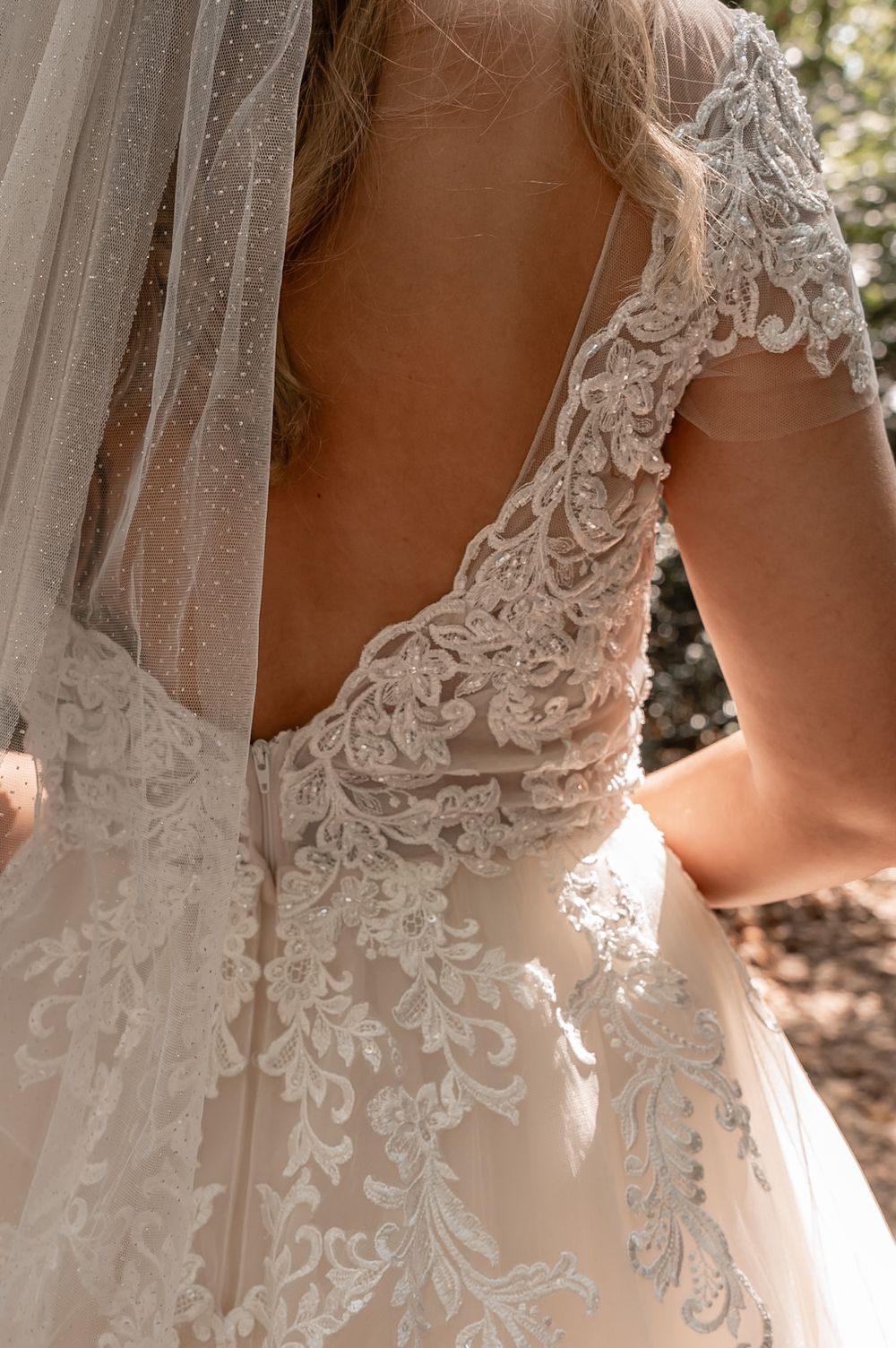 Close-up details of delicate white lace and beading on a wedding dress bodice in natural lighting.