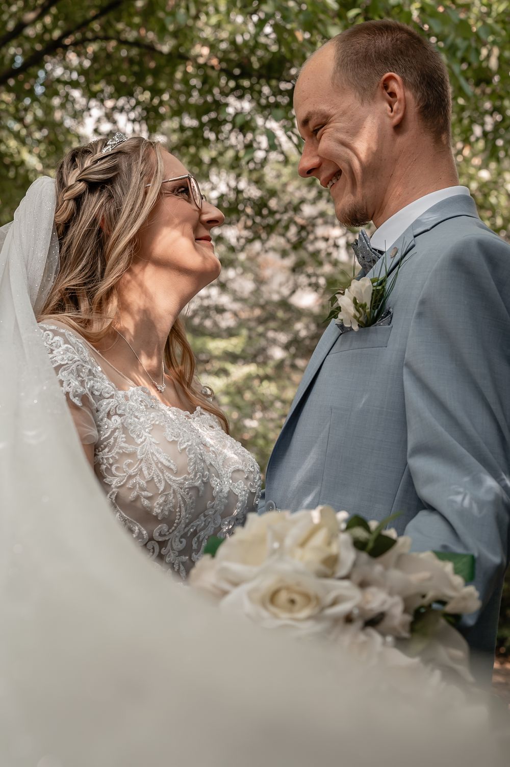 Close-up of wedding couple with white roses and delicate lace details in natural outdoor setting.