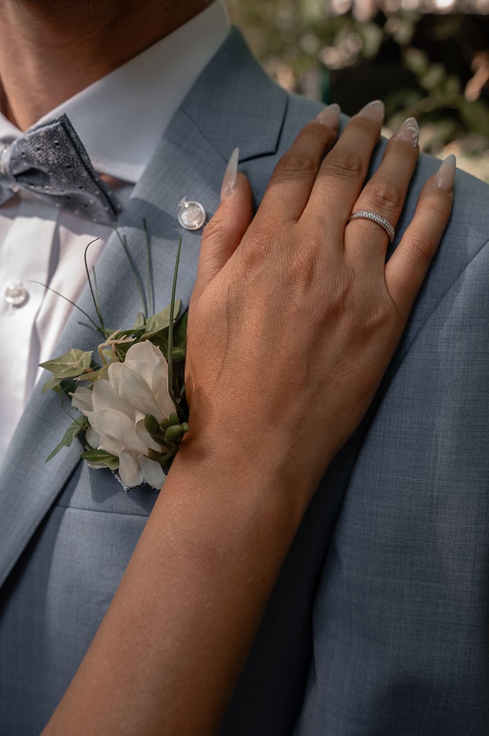 Close-up of hands wearing wedding rings resting on a light blue suit jacket.