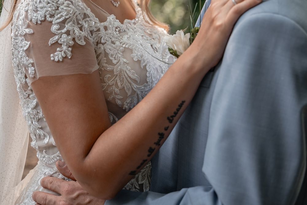 Detail shot of wedding attire showing intricate lace on the bride's dress against a gray suit.