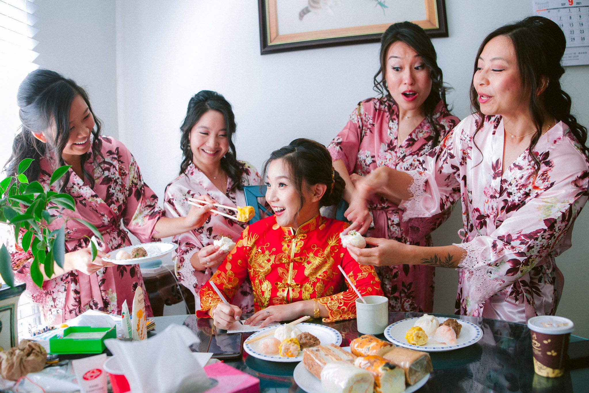 A group wearing matching pink floral robes gathers around a table enjoying a meal together.