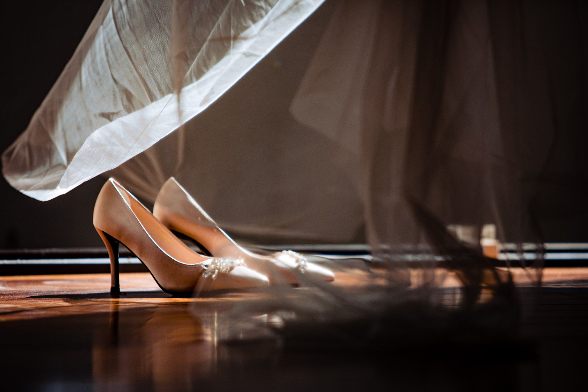 Close-up details of elegant white wedding shoes and dress hem in dramatic lighting.