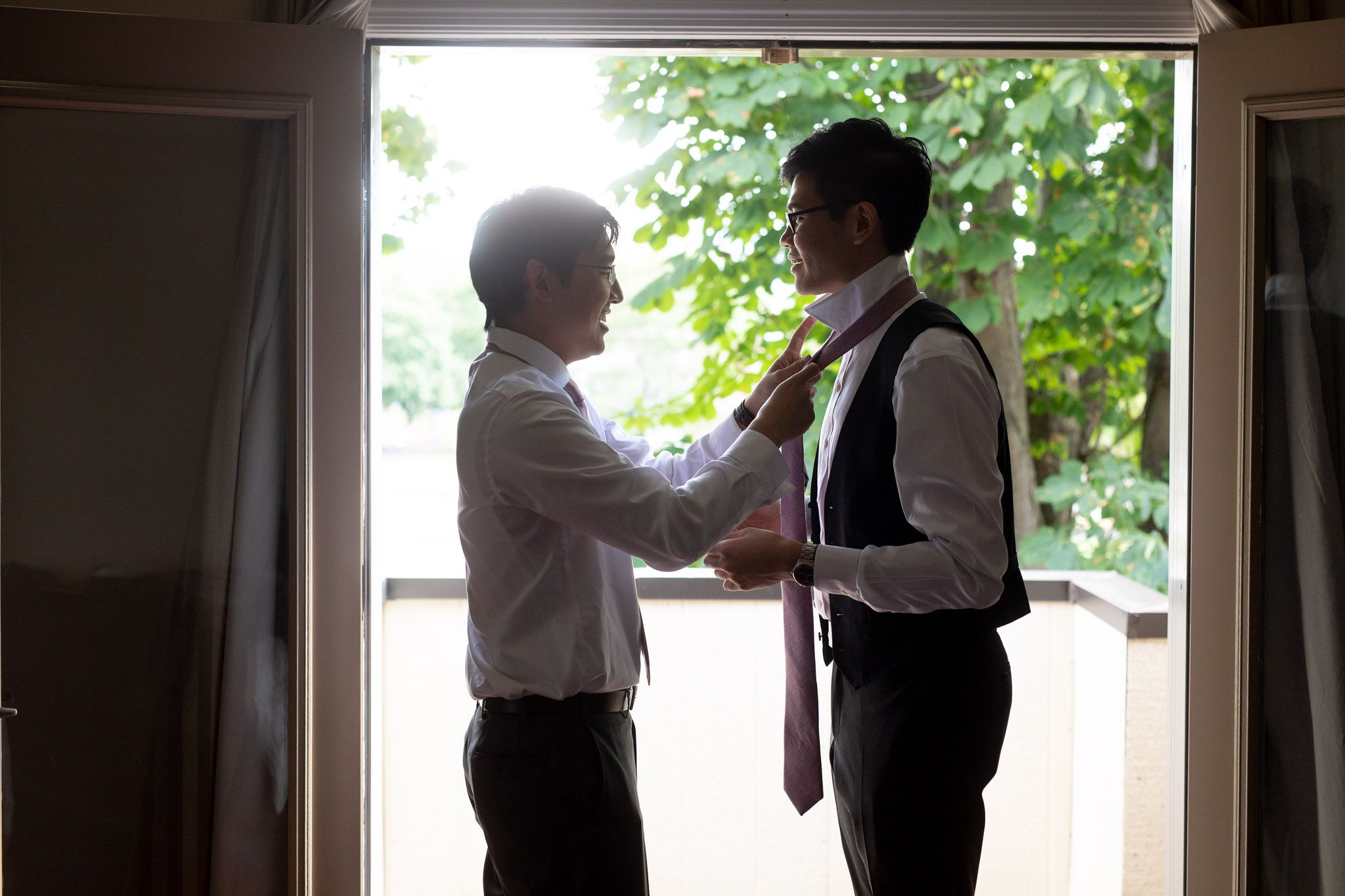 People in formal attire interacting in a sunlit indoor space with windows.