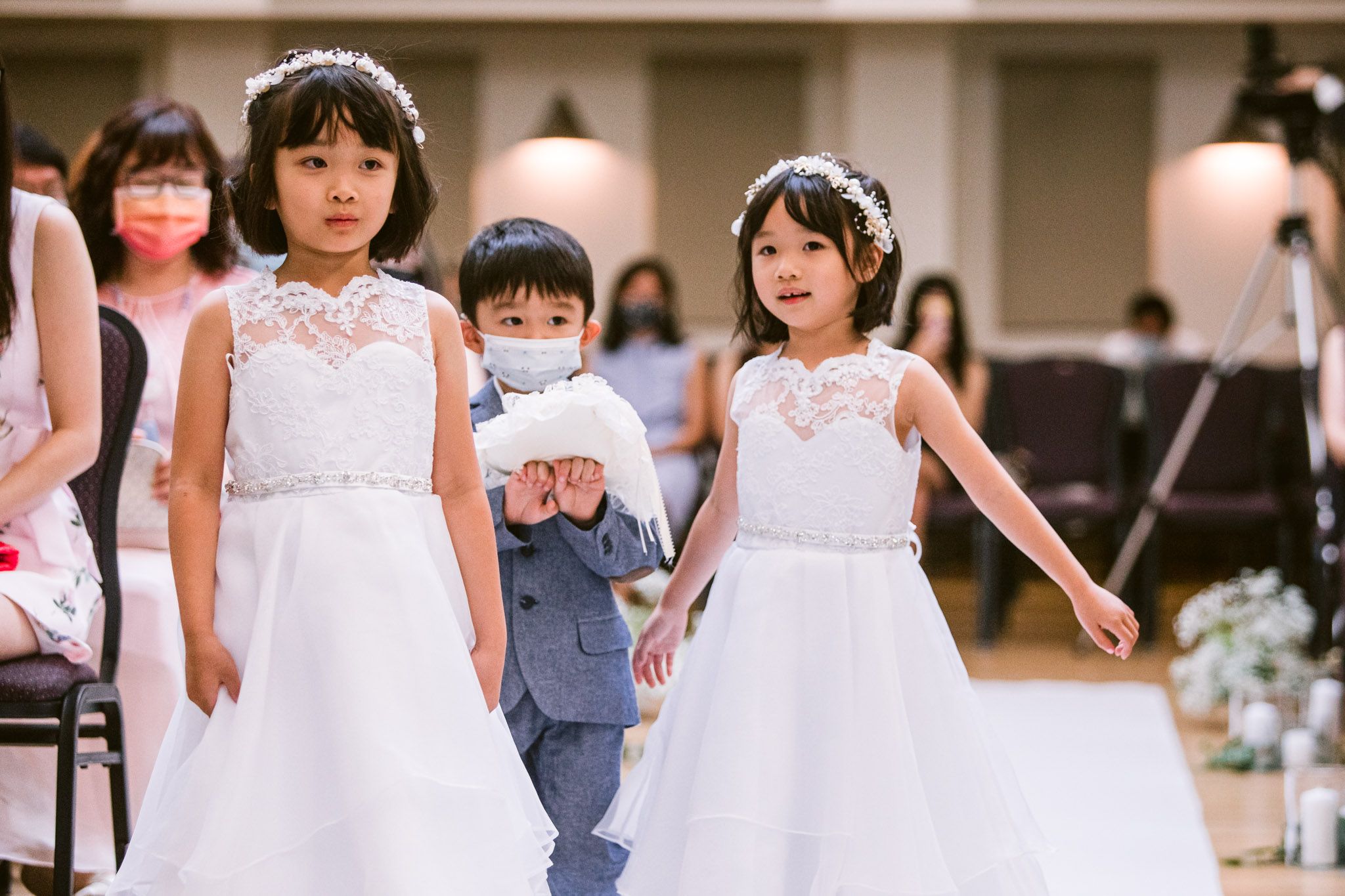 Young children in white formal attire walking down an aisle at an elegant wedding ceremony.