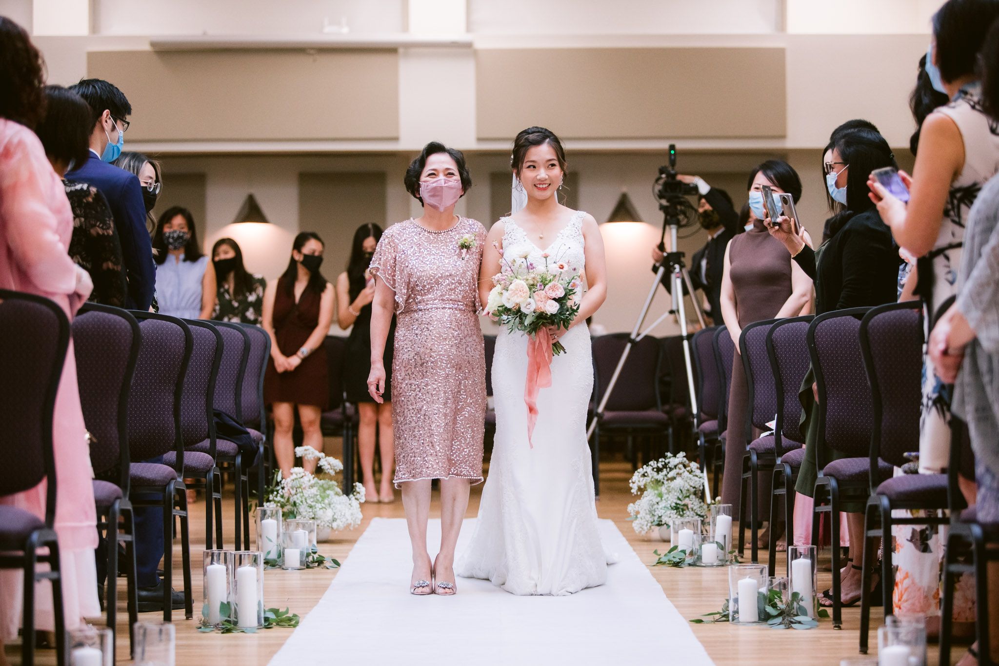 Wedding ceremony in a formal hall with rows of chairs and floral decorations.