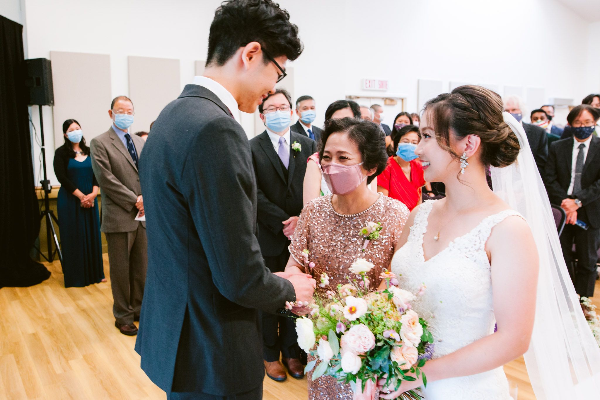 Wedding ceremony in a bright white room with guests watching the couple exchange vows.