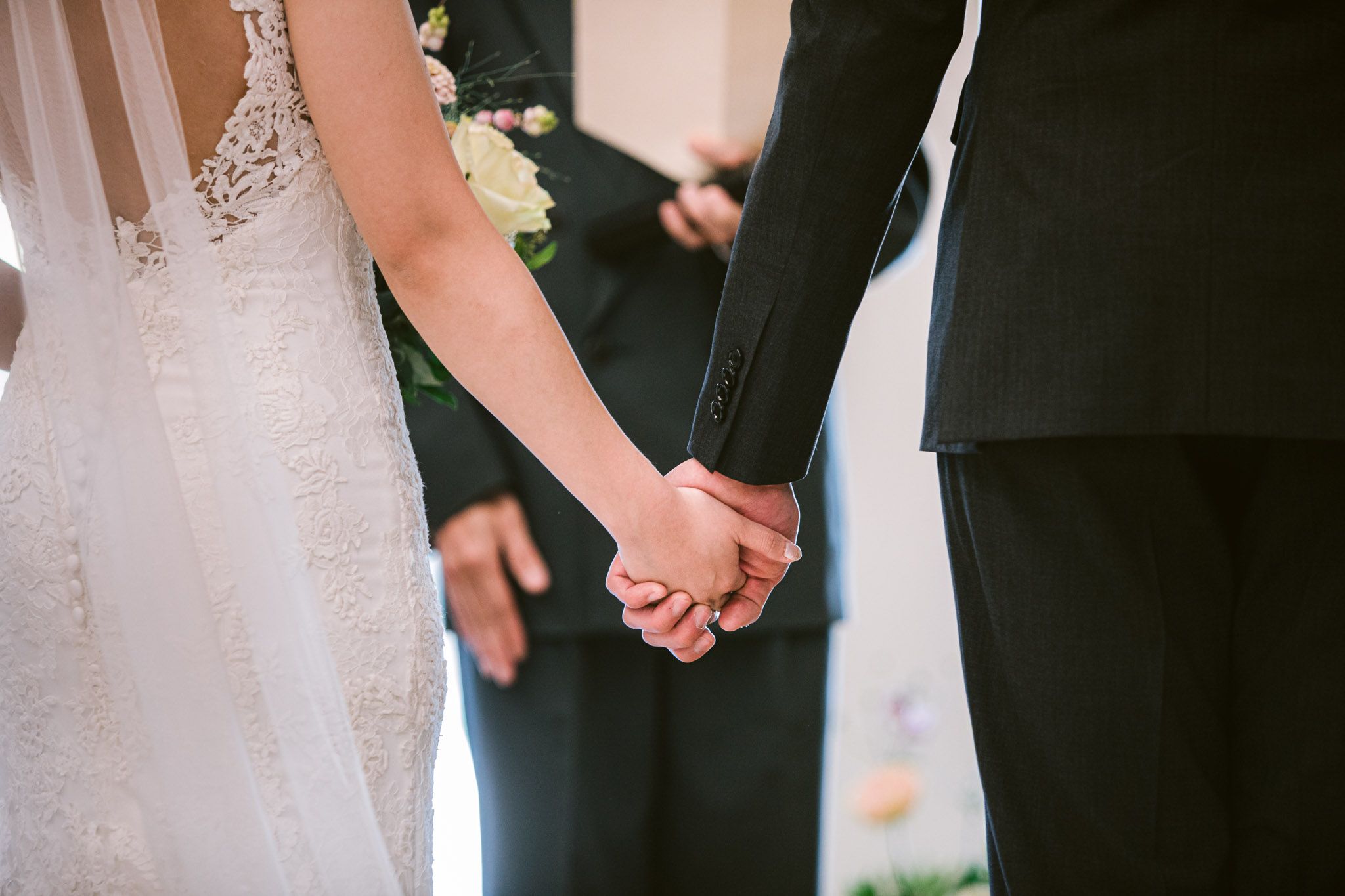A couple holds hands during their wedding ceremony while wearing formal attire.