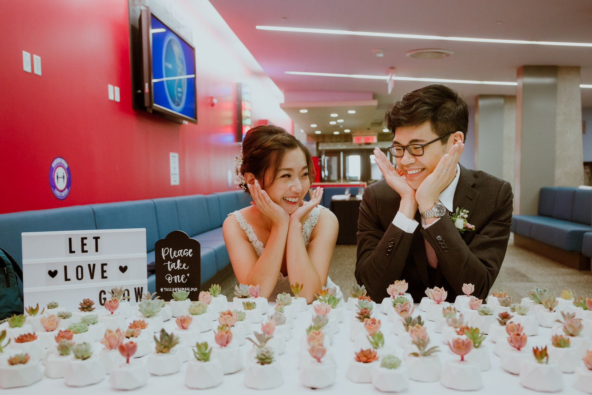 A couple poses at their wedding reception behind a display of small desserts with a 'Let Love' sign.