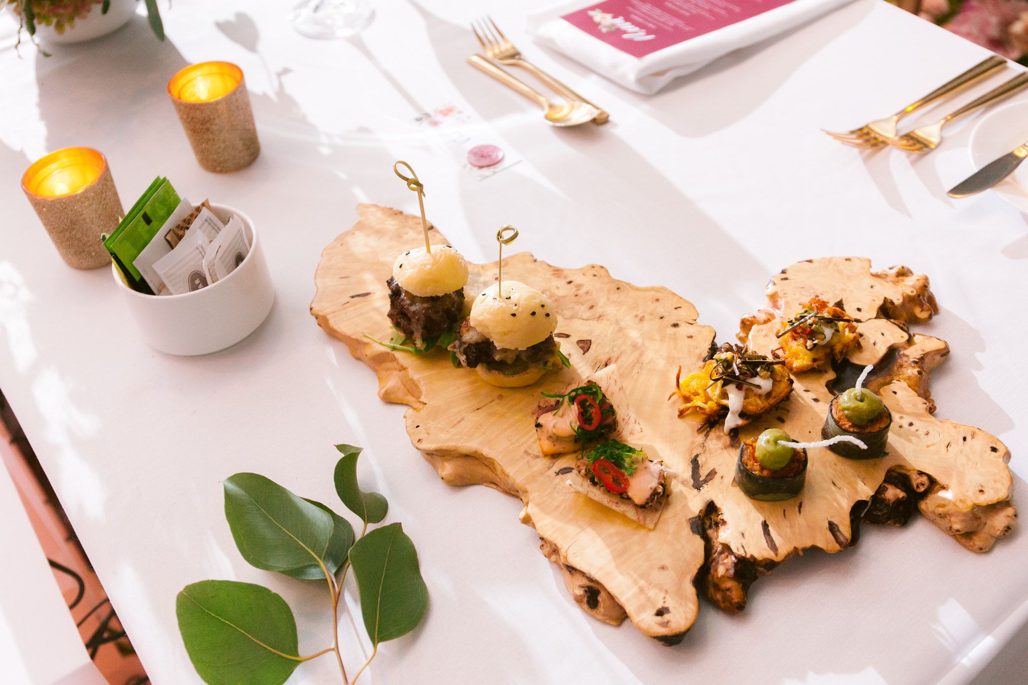 Elegant white wedding reception table settings with scattered greenery and plated food.