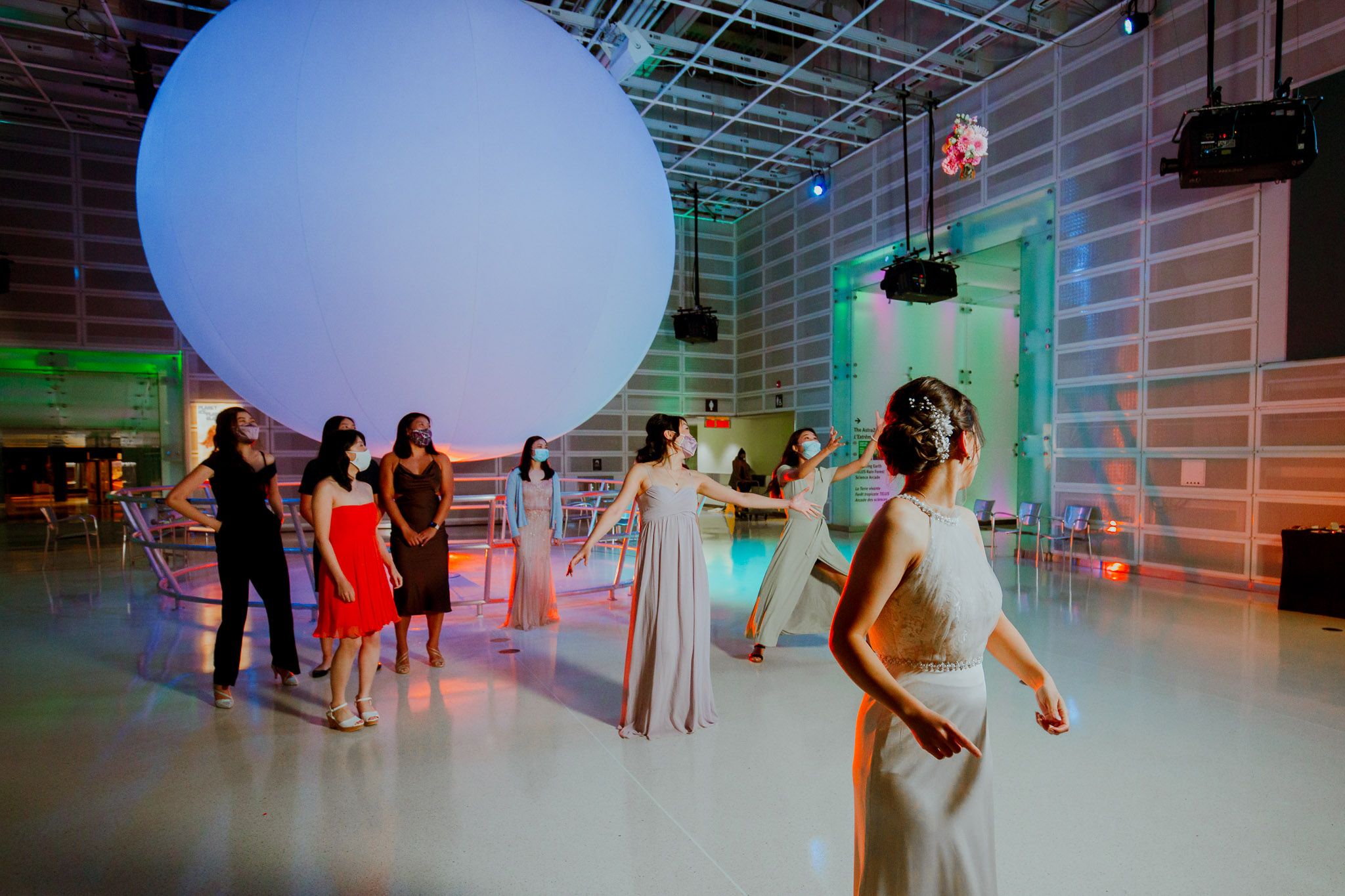 People dancing and celebrating at an indoor event space with a giant white balloon and colorful lighting effects.