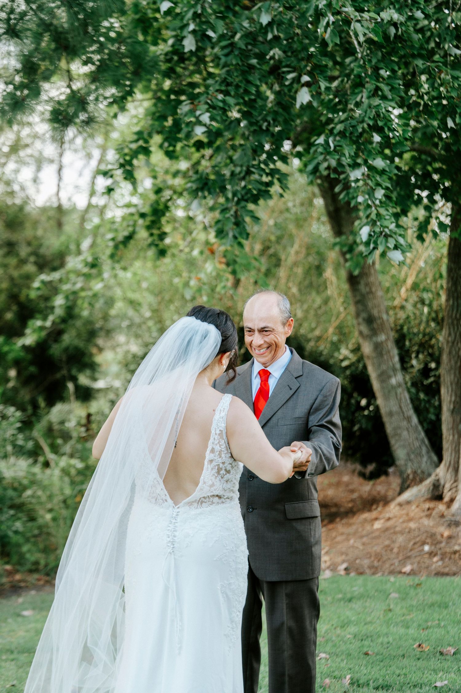 A bride and groom share a romantic moment outdoors under green trees during their wedding photoshoot.