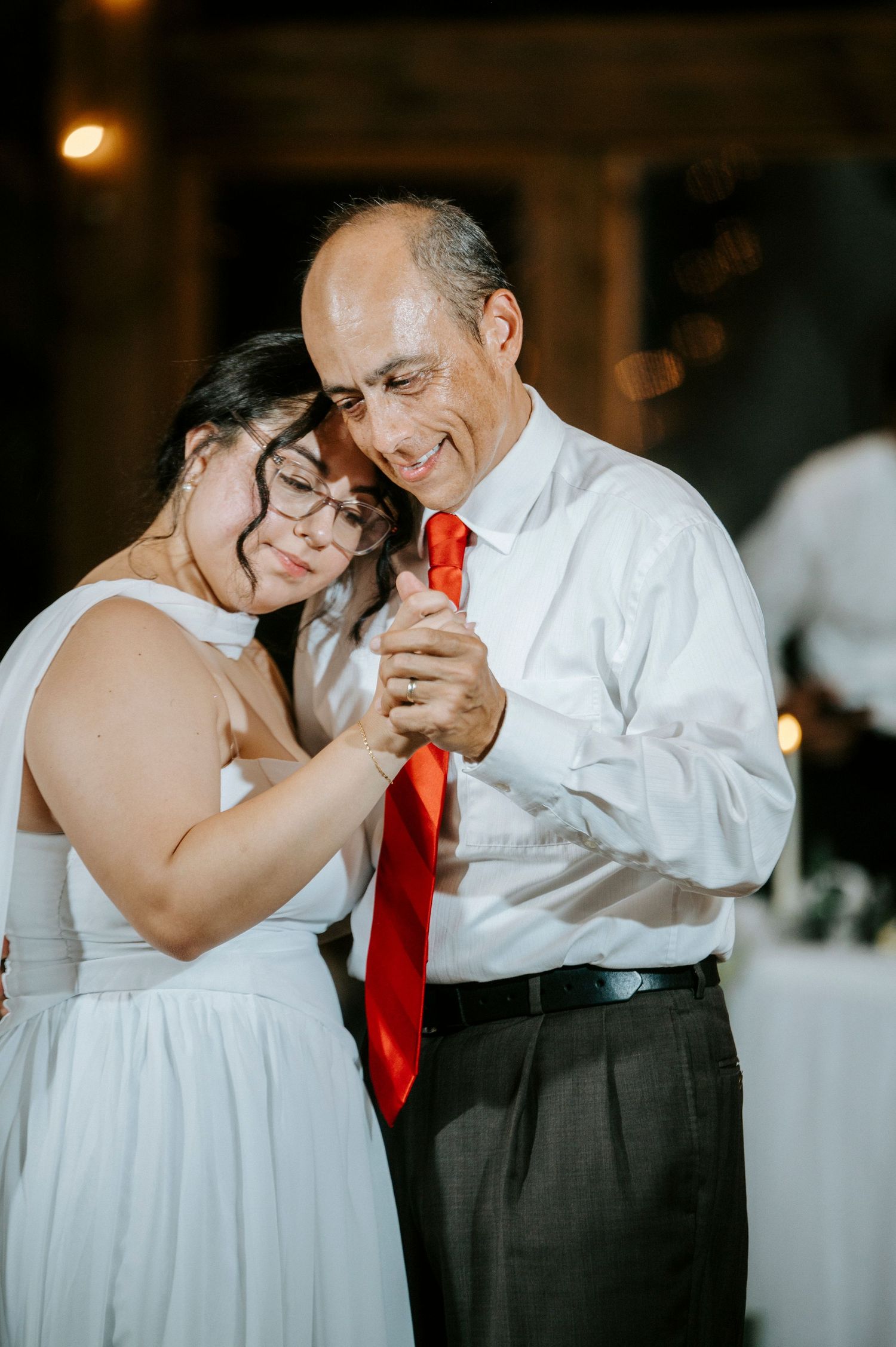 A tender father-daughter dance moment at a wedding reception shows emotional embrace in warm lighting.
