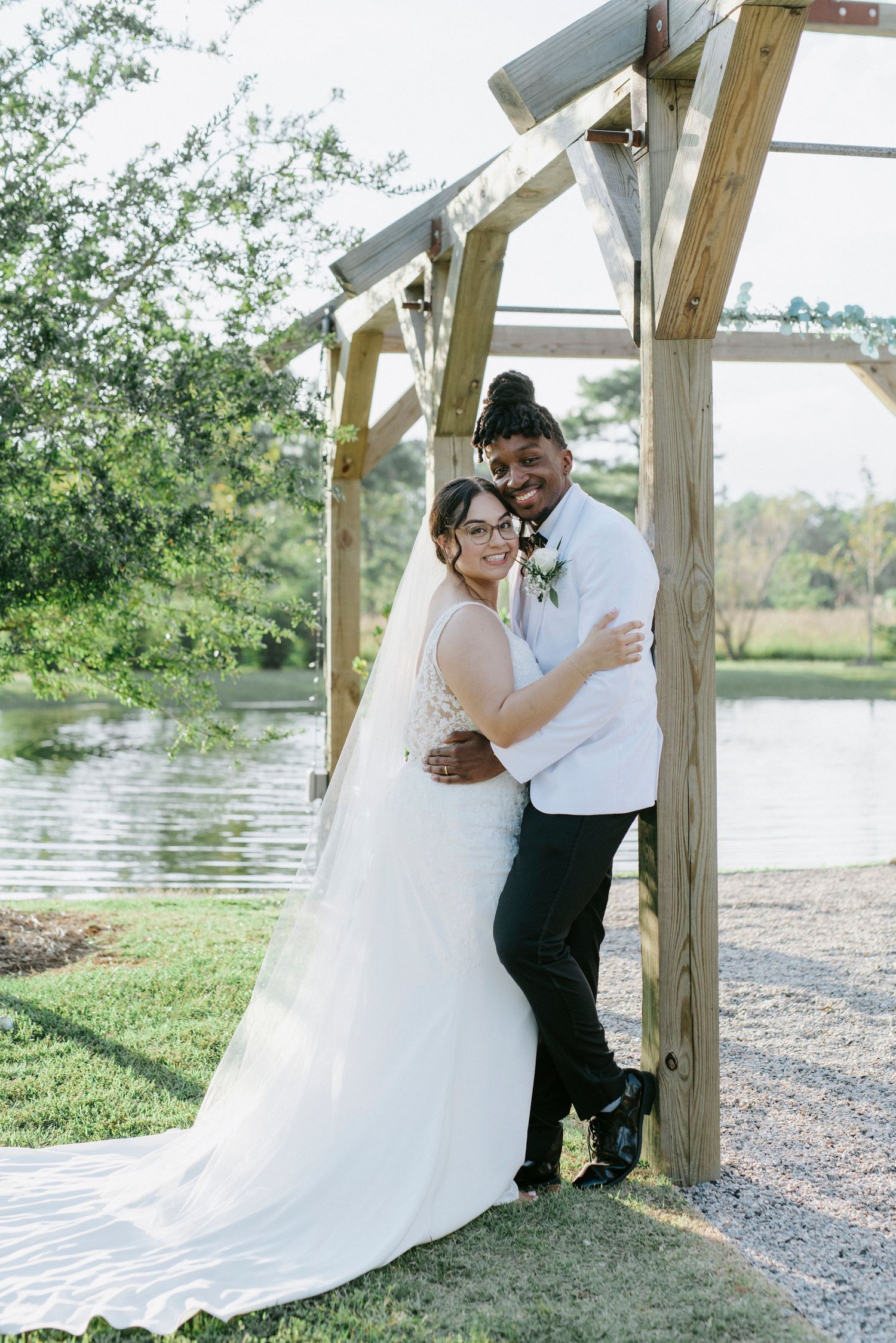 A couple shares intimate moments under a wooden gazebo by a serene lakeside on their wedding day.