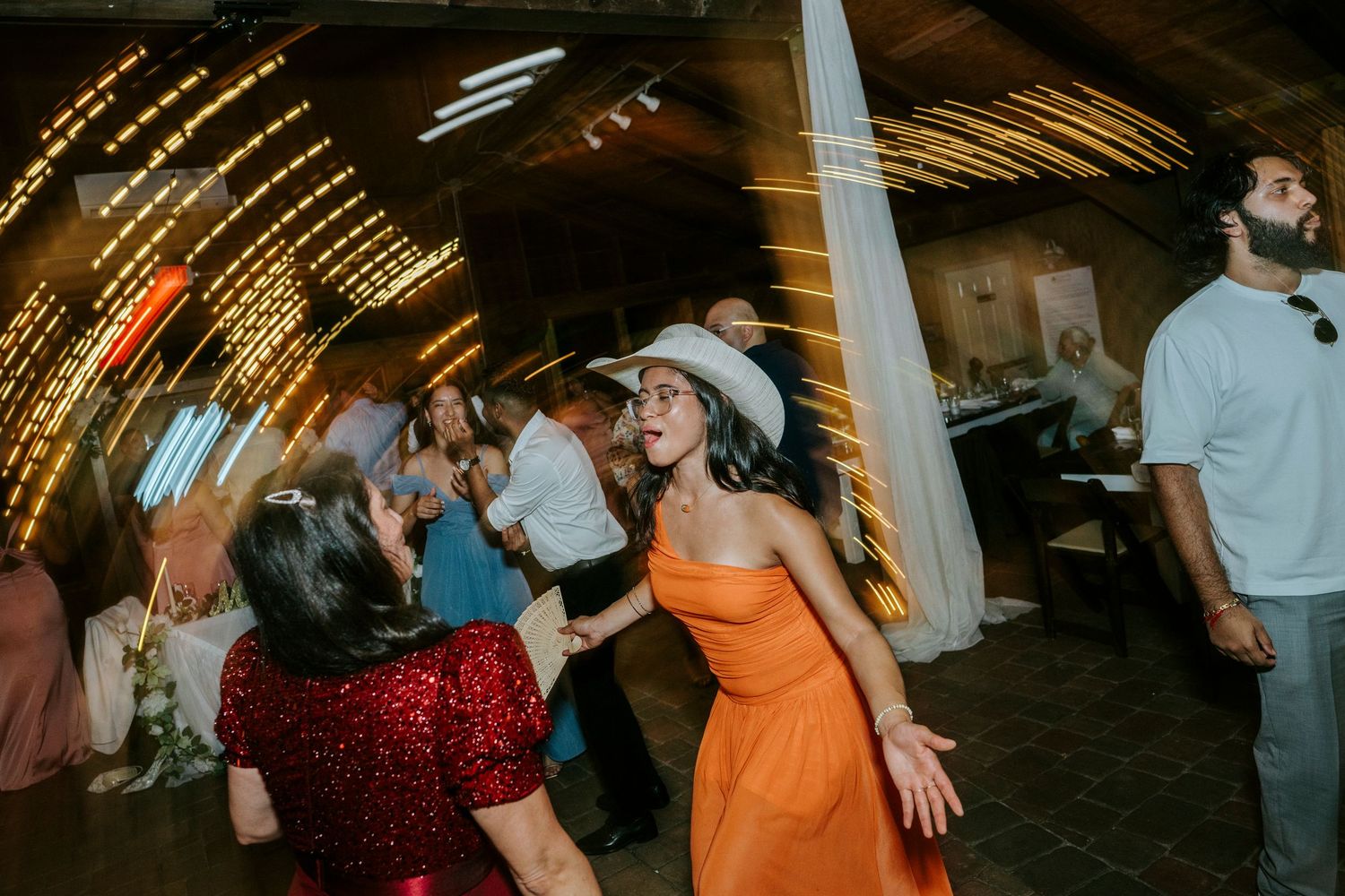 People dancing and celebrating at a lively party with warm lighting and rustic wooden ceiling beams.