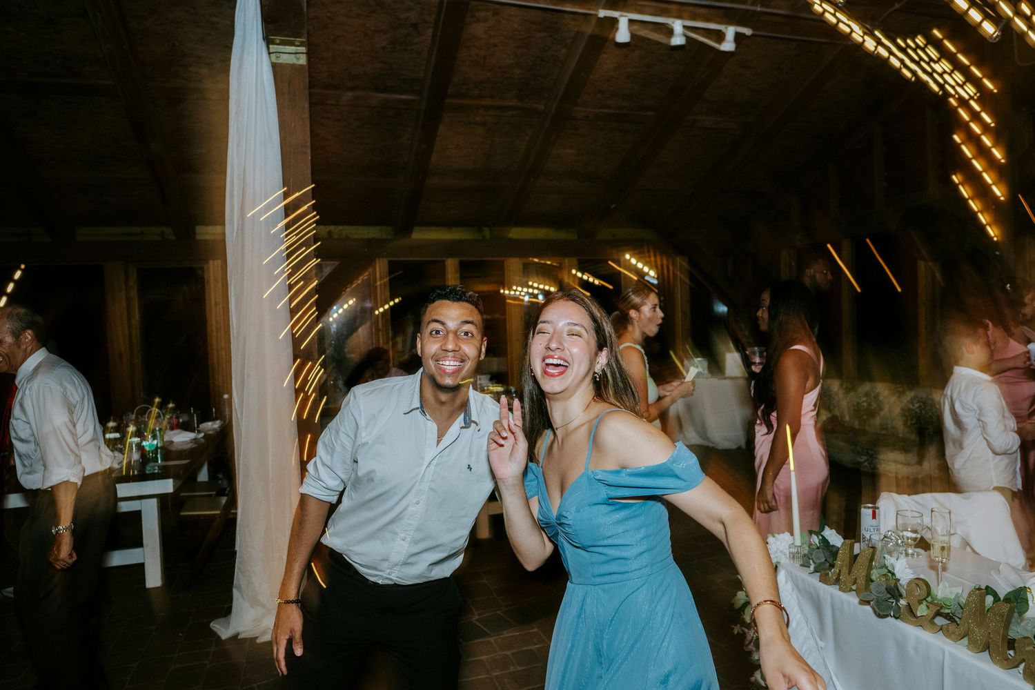 Guests enjoying a lively dance party at an indoor wedding reception with decorative lighting.