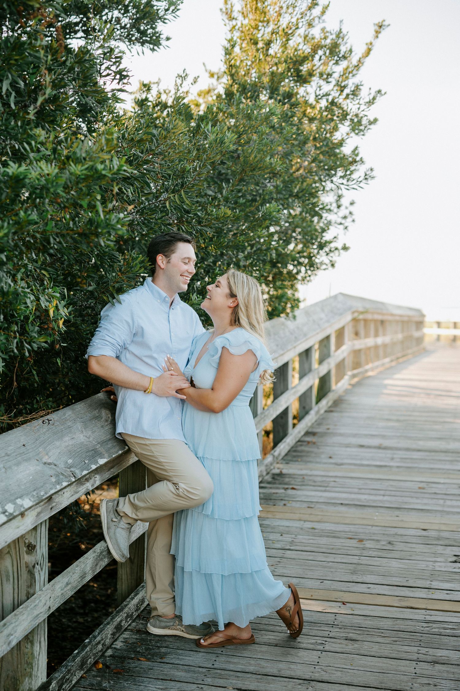 A couple shares a romantic moment on a wooden boardwalk surrounded by lush greenery during golden hour.