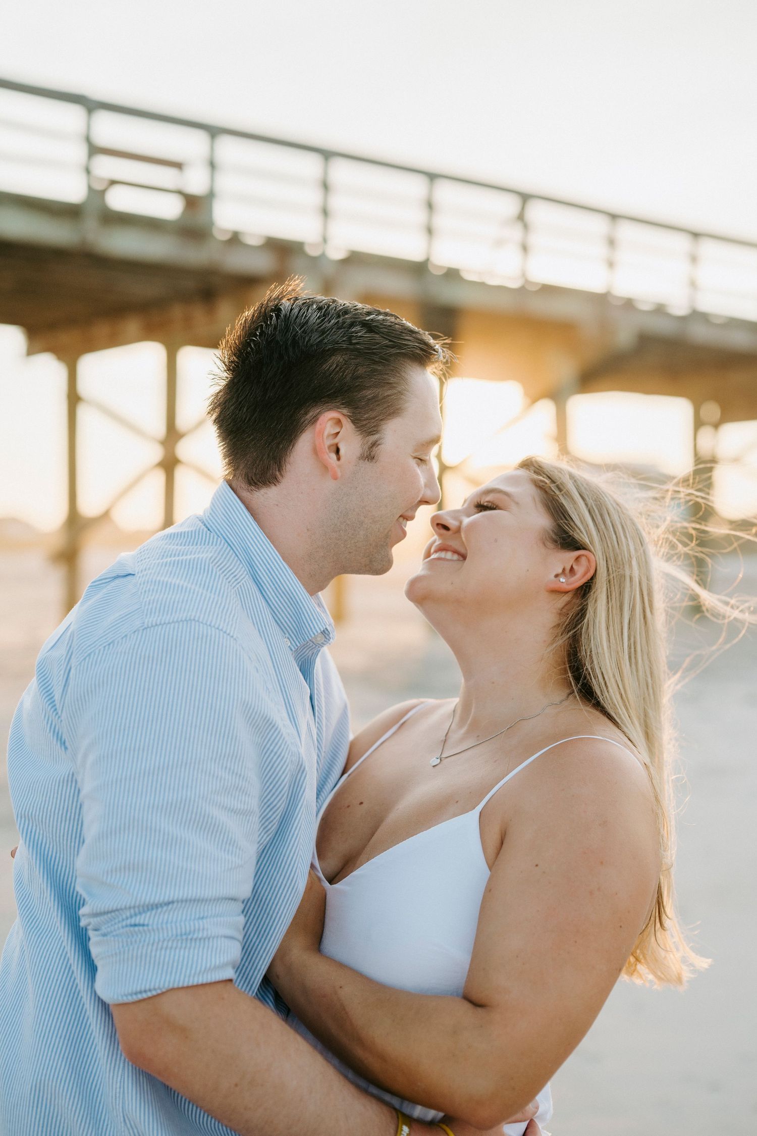 A romantic couple shares an intimate moment at sunset under a bridge, with golden light illuminating their embrace.