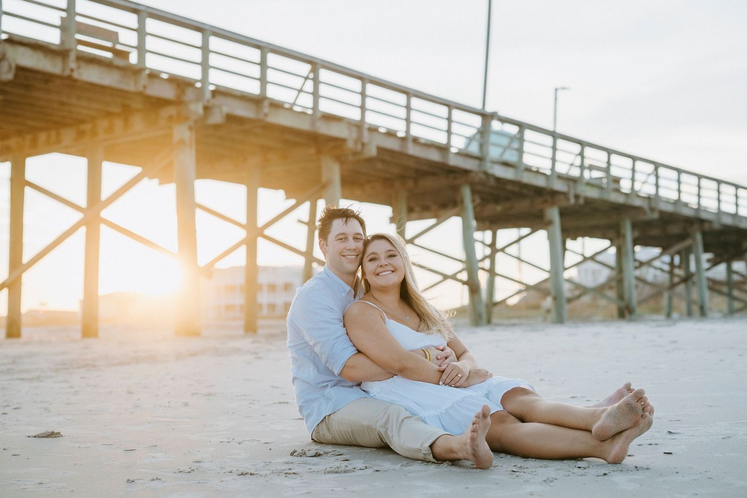 Couple enjoying romantic sunset on beach near pier during engagement photo session.