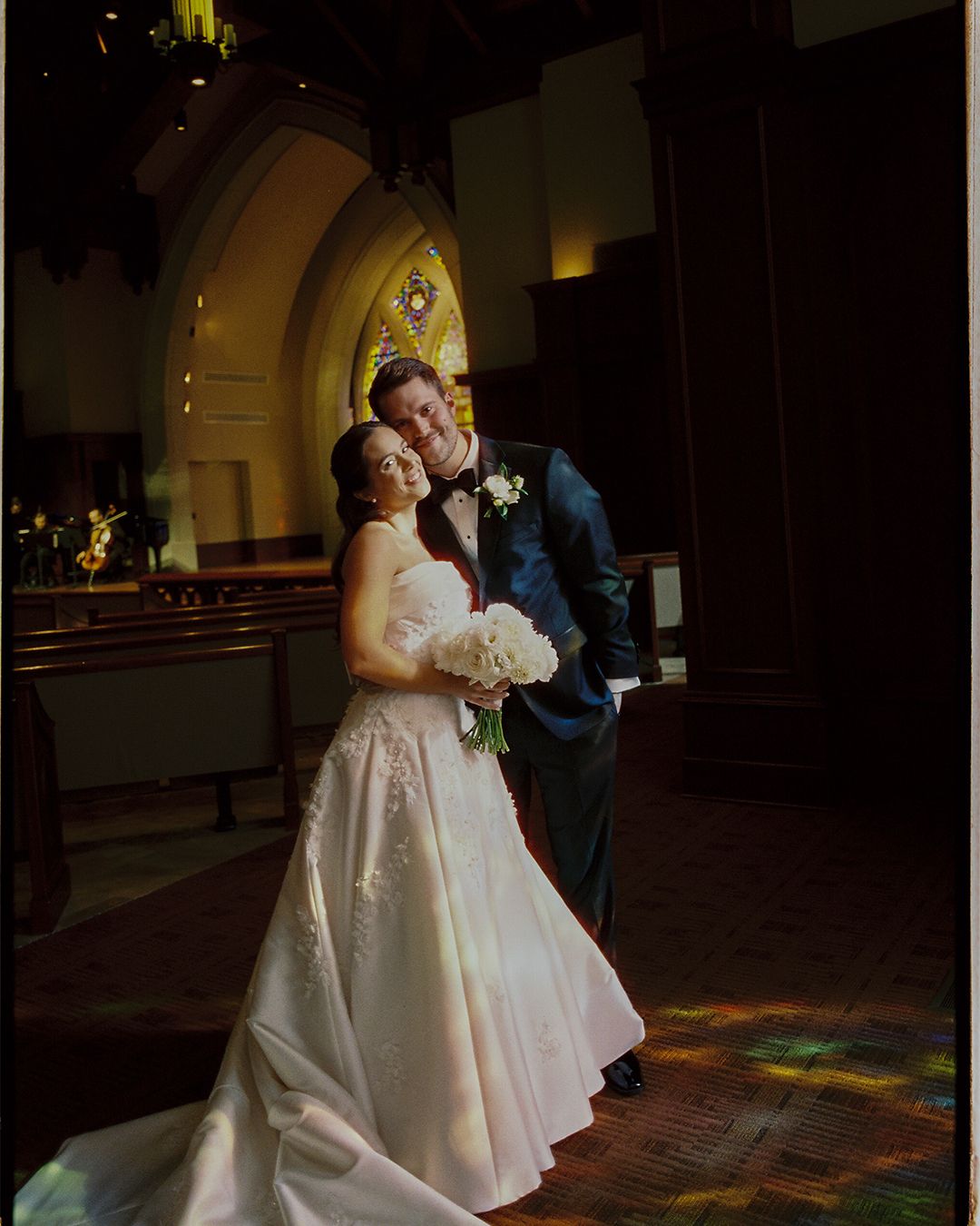 Couple dancing in a church with stained glass windows casting colorful light on the floor during their wedding celebration.