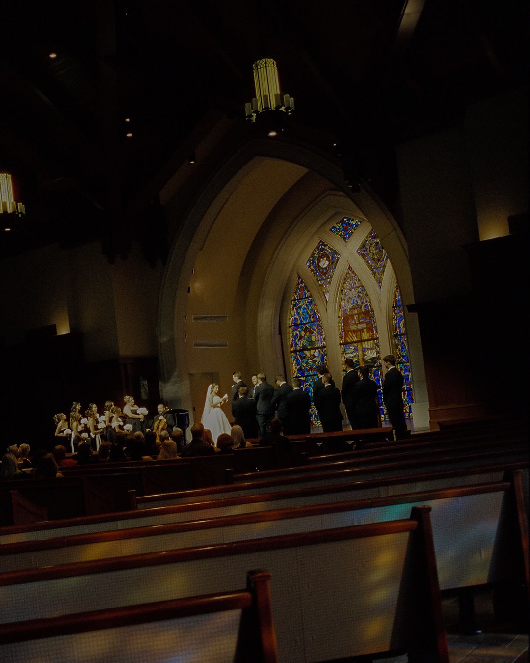 Choir members perform in traditional white robes inside a church sanctuary with stained glass windows.