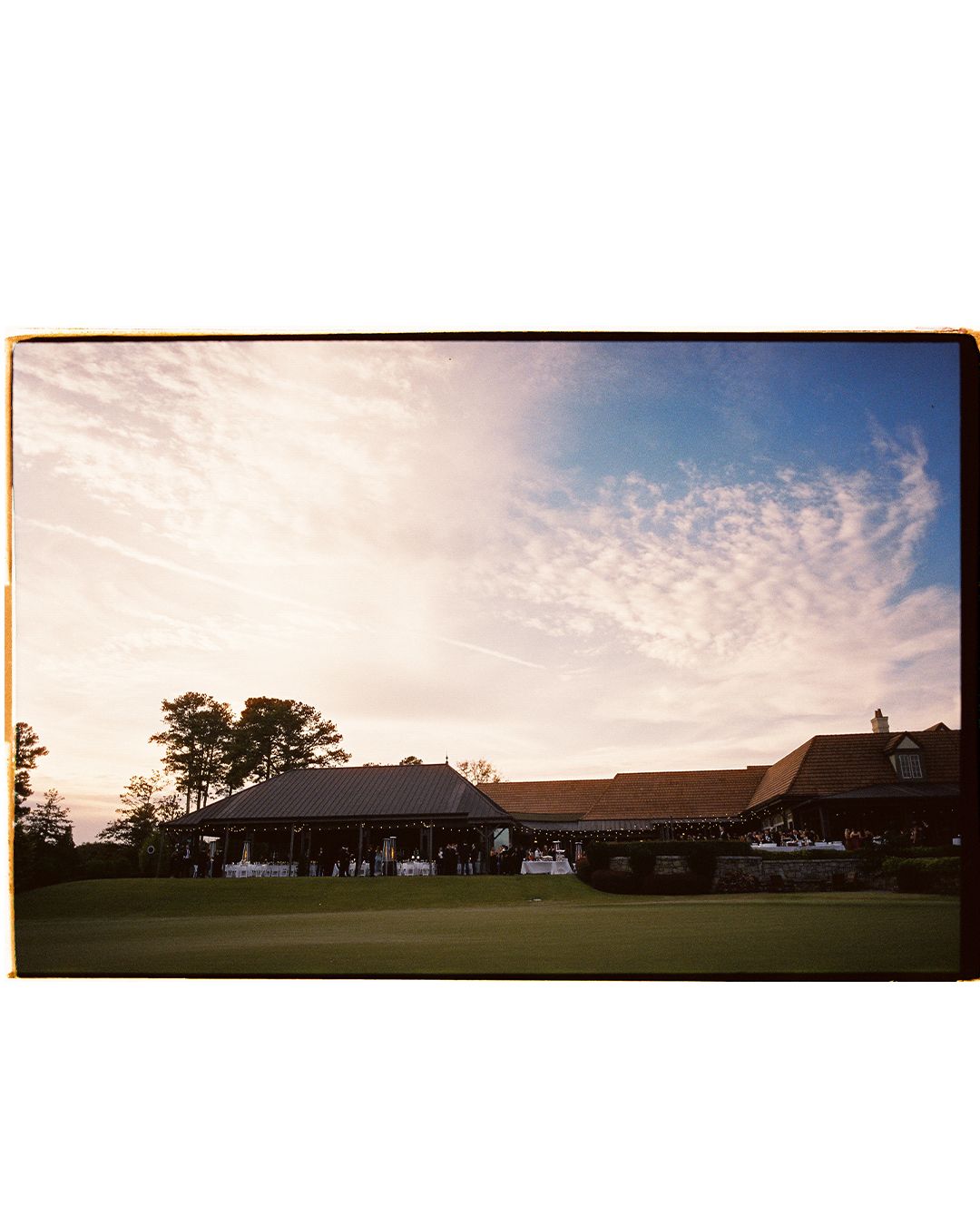 Panoramic view of a golf course at sunset with trees silhouetted against an orange and pink sky.