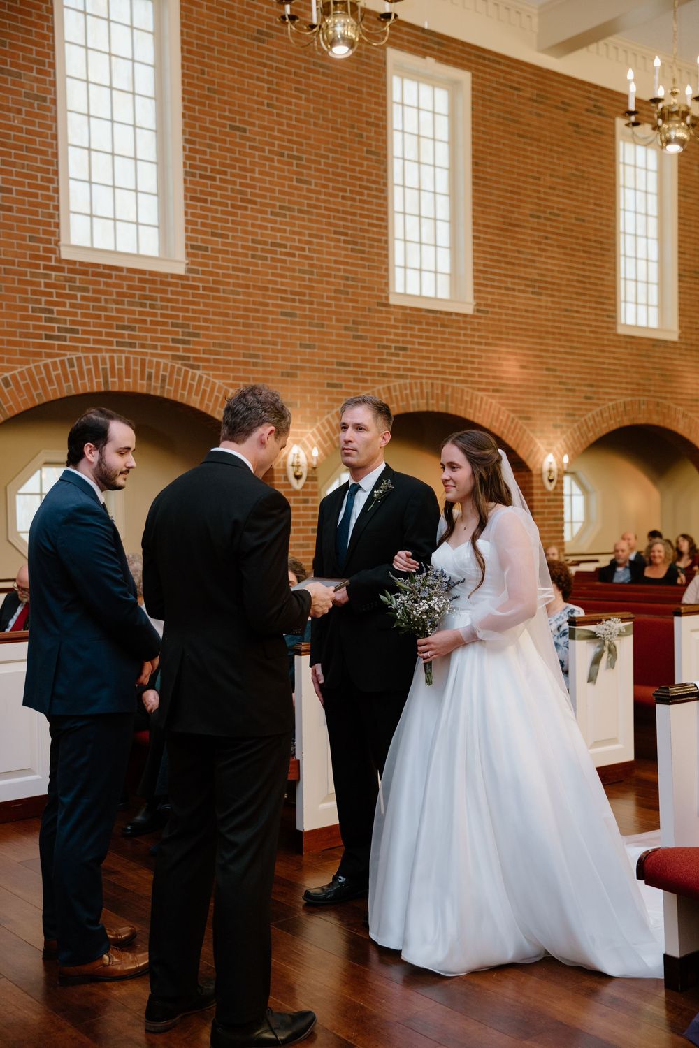 Wedding ceremony candid moments inside traditional brick church with arched windows.