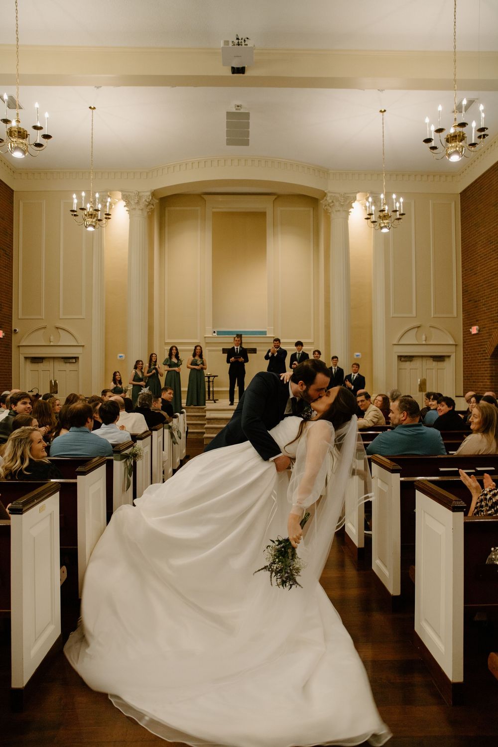 A wedding reception venue with elegant chandeliers and white-draped chairs arranged in rows.