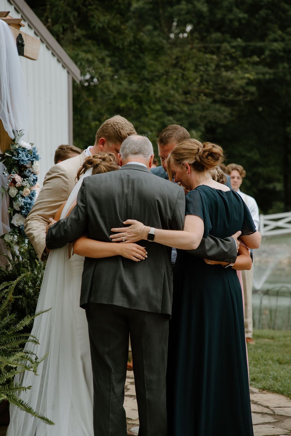 Wedding party members embrace in a group hug outdoors.