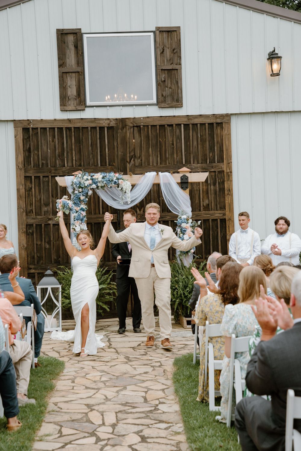 Wedding ceremony exit with guests lined up along a stone pathway outside a white barn.