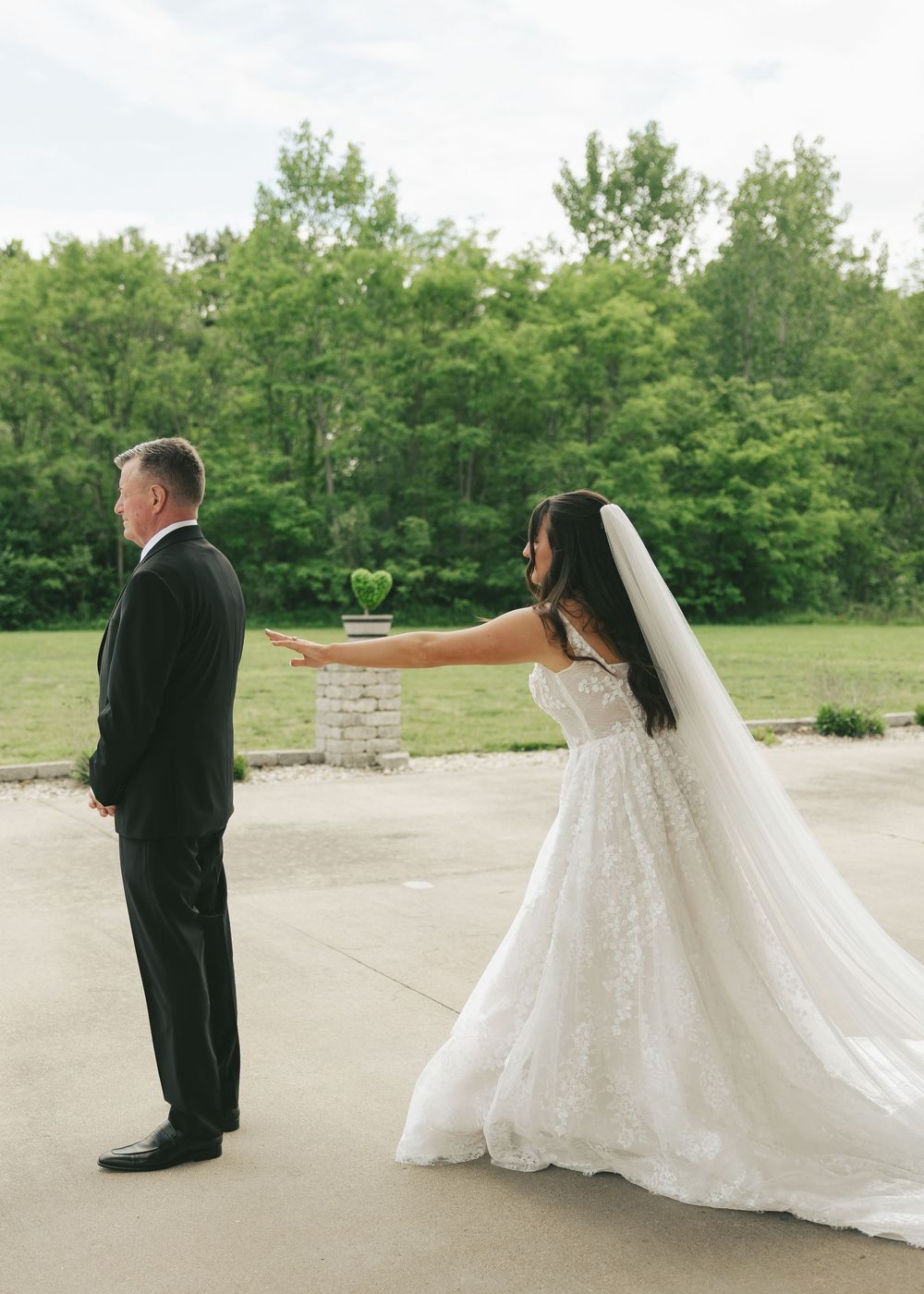 Bride in lace gown and veil taps groom on shoulder during an emotional first look moment on a patio.