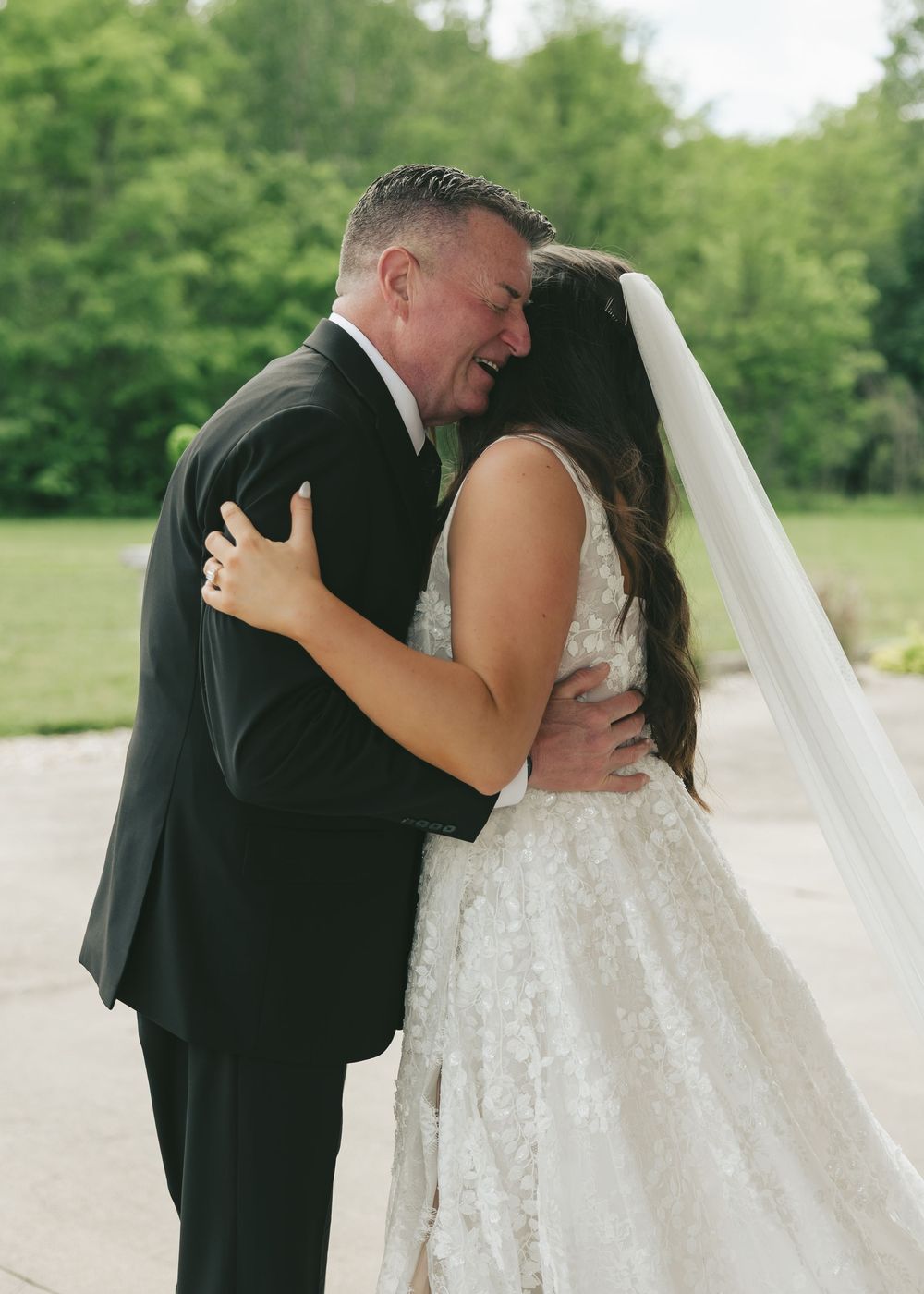 Bride and older man share an emotional first look hug outdoors at a wedding ceremony.