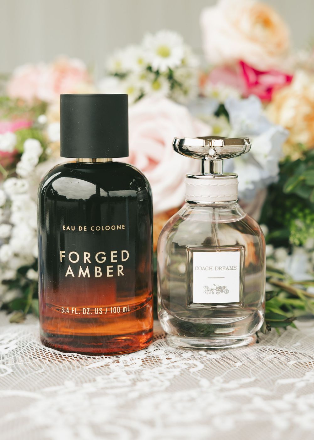 Forged Amber cologne and Coach Dreams perfume displayed with pink roses for a wedding flat lay.