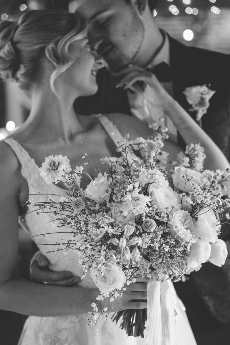 A black and white wedding celebration scene with guests throwing confetti at a couple outside a brick building.