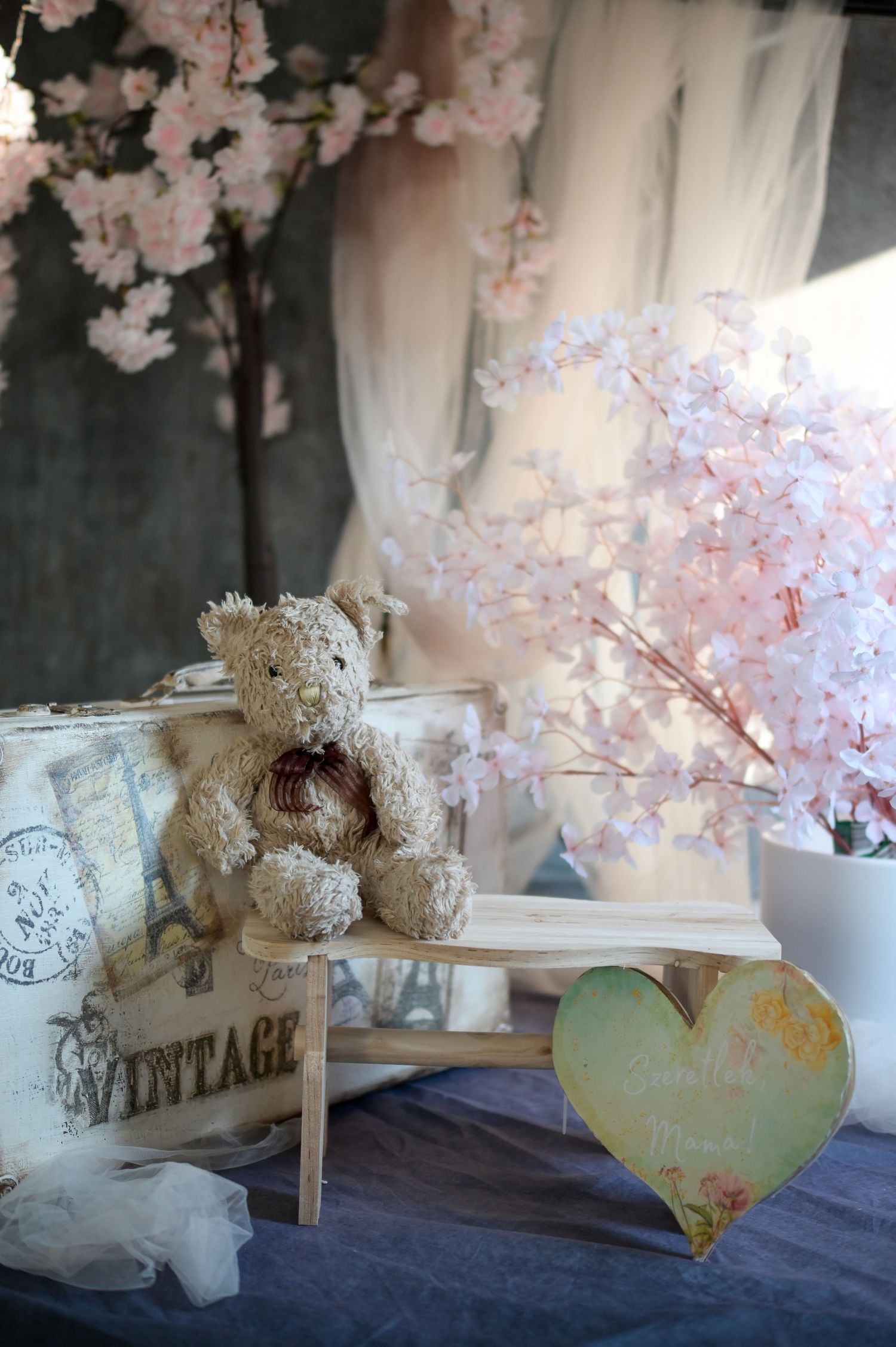Vintage wedding decor display with pink cherry blossoms, teddy bear, and rustic signage on navy blue tablecloth.