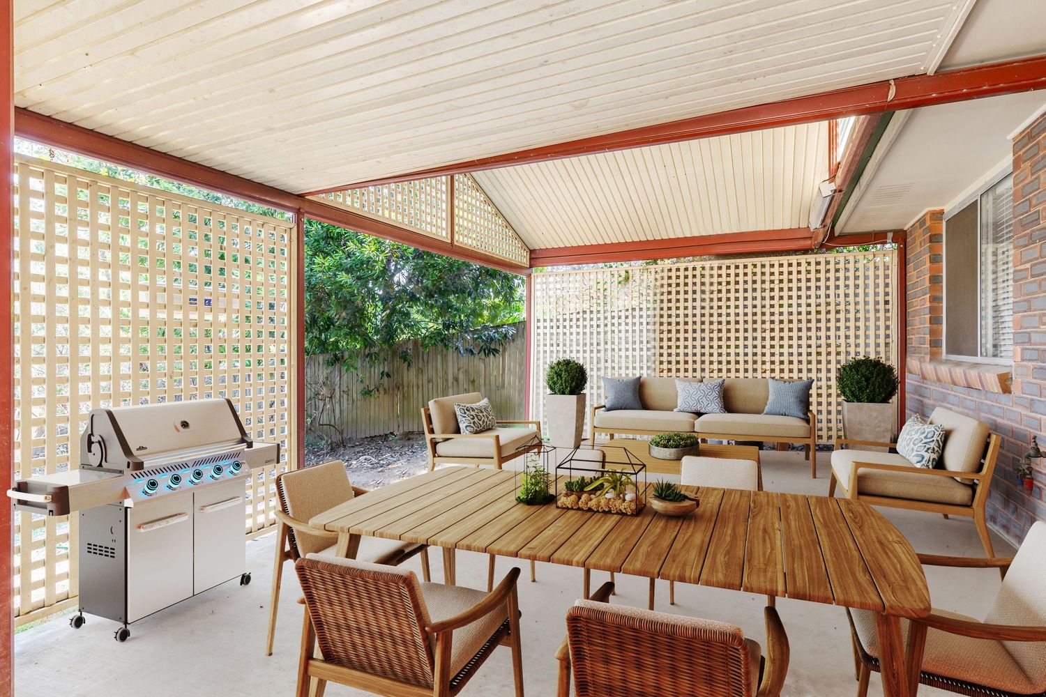 Alfresco entertaining area with timber dining table, outdoor sofa, barbecue grill, and decorative lattice screening.