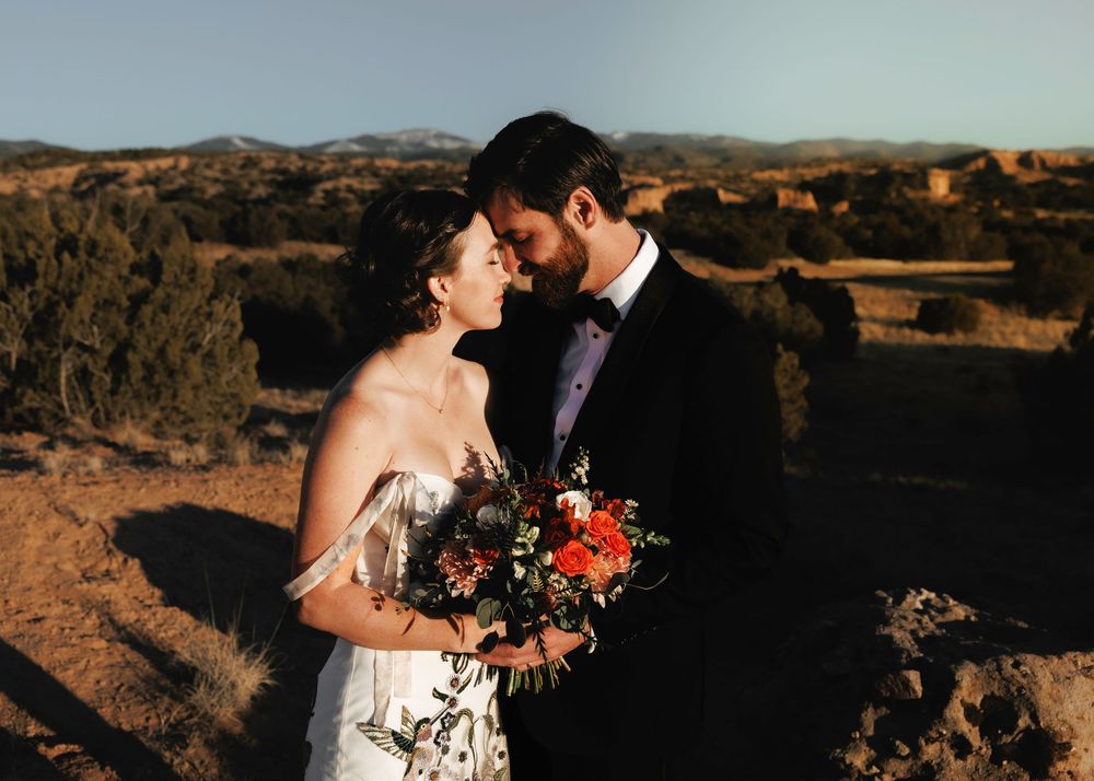 Bride and groom nearly kissing outdoors, bride holding autumn bouquet with mountain views.