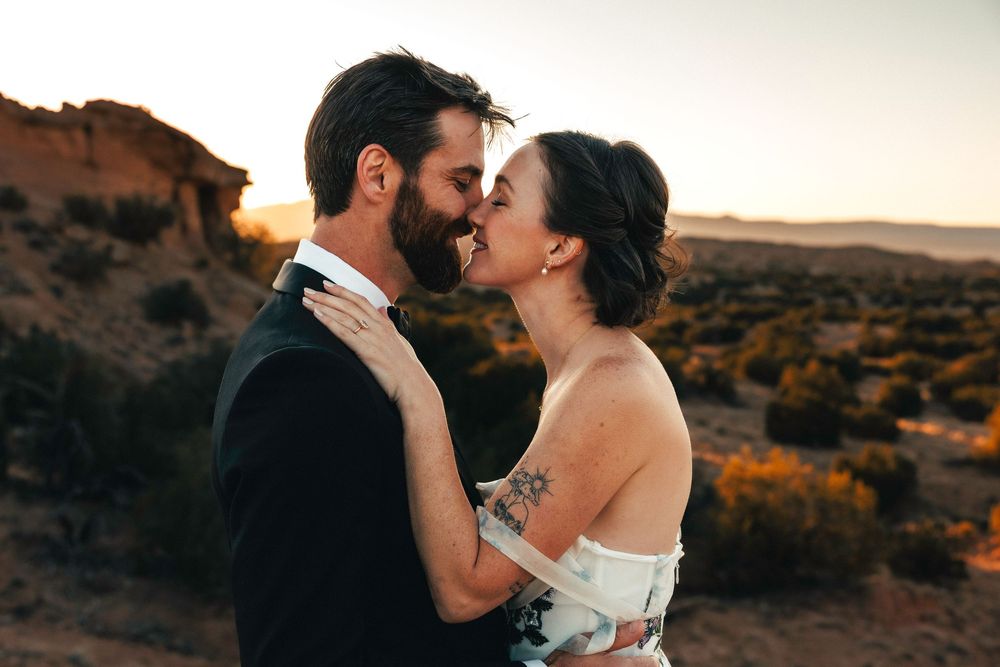 Bride and groom share an intimate moment, nearly kissing, in a desert landscape at golden hour.