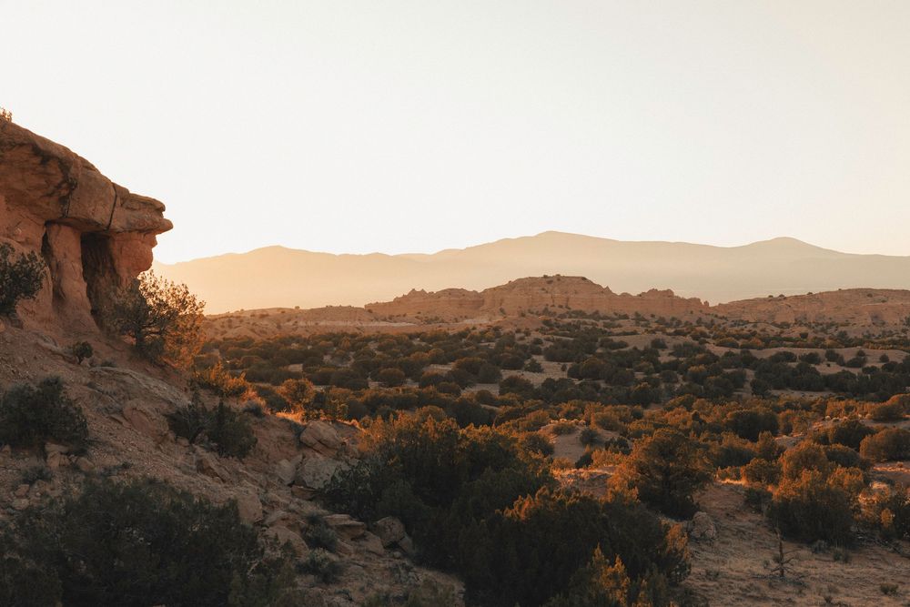 Warm golden sunset over a vast desert landscape with red rock formations and mountains.