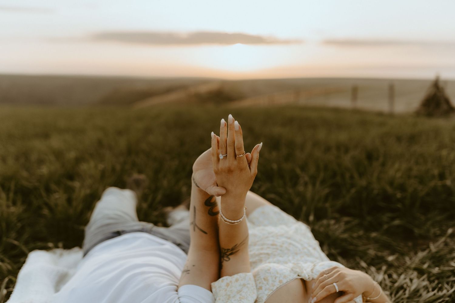 Couple walking through golden field at sunset with mountains in distance.