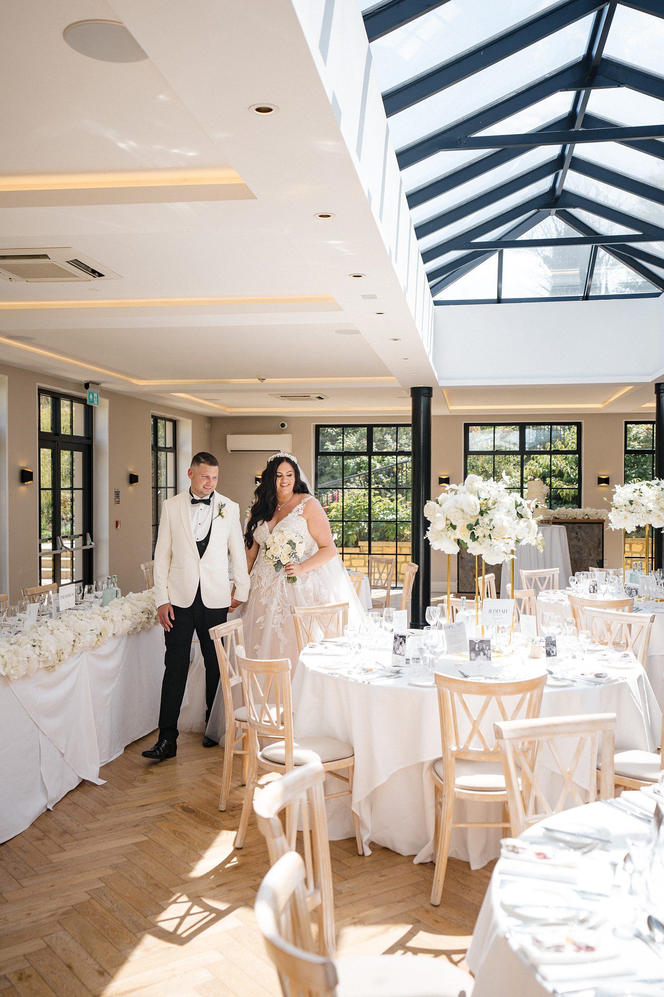 Elegant wedding reception venue with white tables, glass skylights, and natural light streaming through large windows.