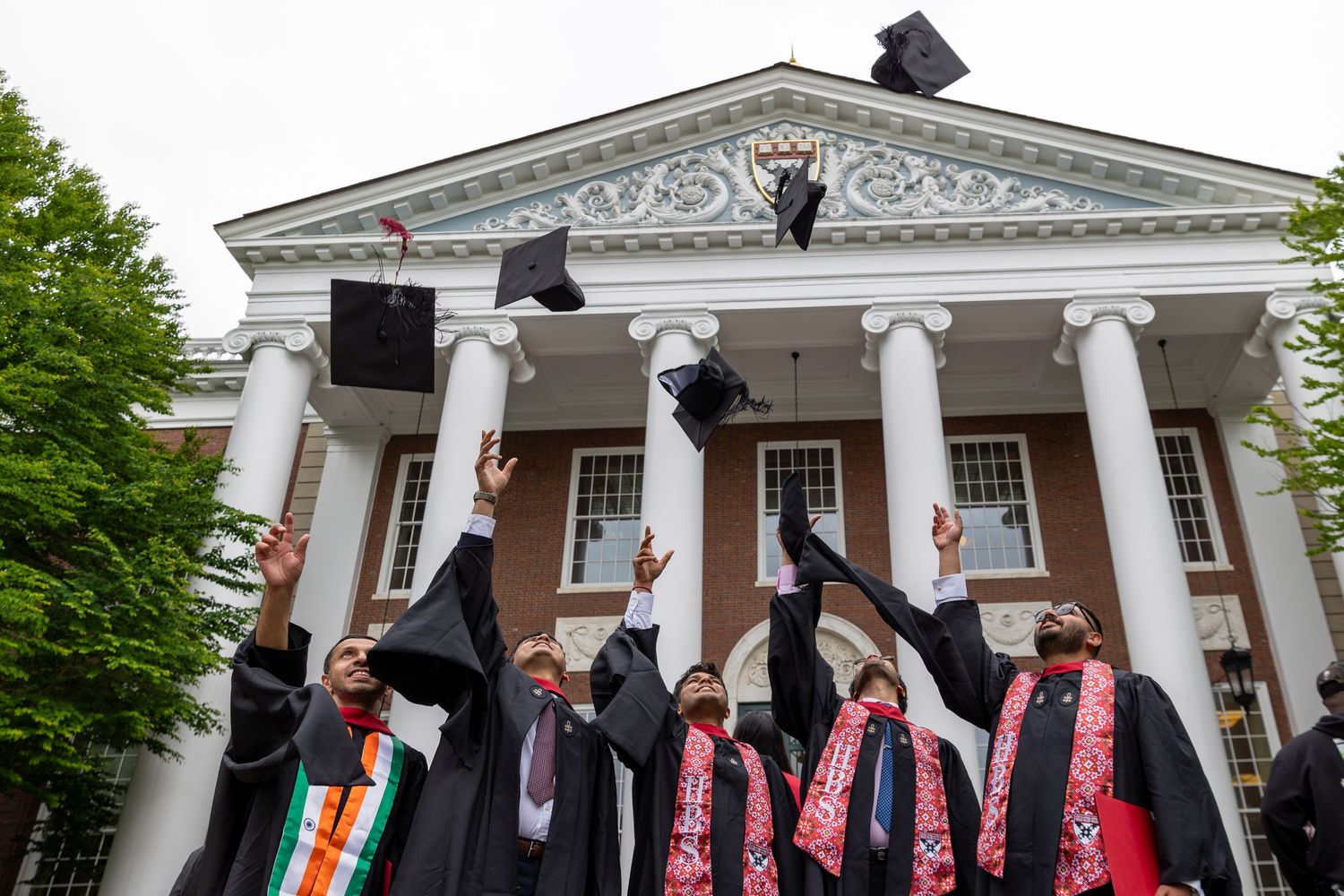 Graduates throw caps in celebration in front of classical building with white columns.