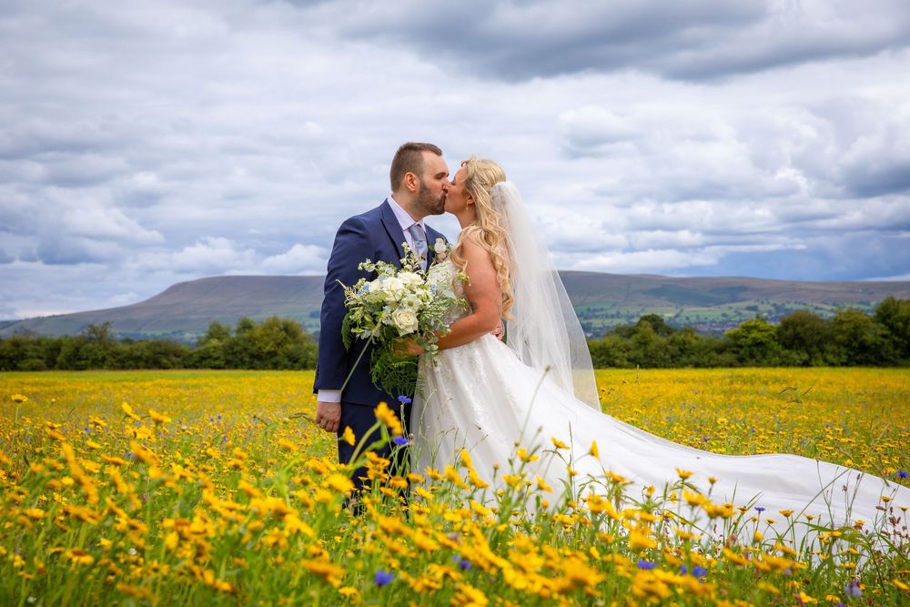 Bride and groom sharing a romantic kiss in a stunning yellow wildflower field with mountain backdrop.