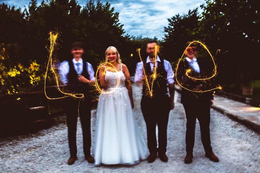 Wedding party writing LOVE with sparklers in magical evening outdoor celebration photograph.