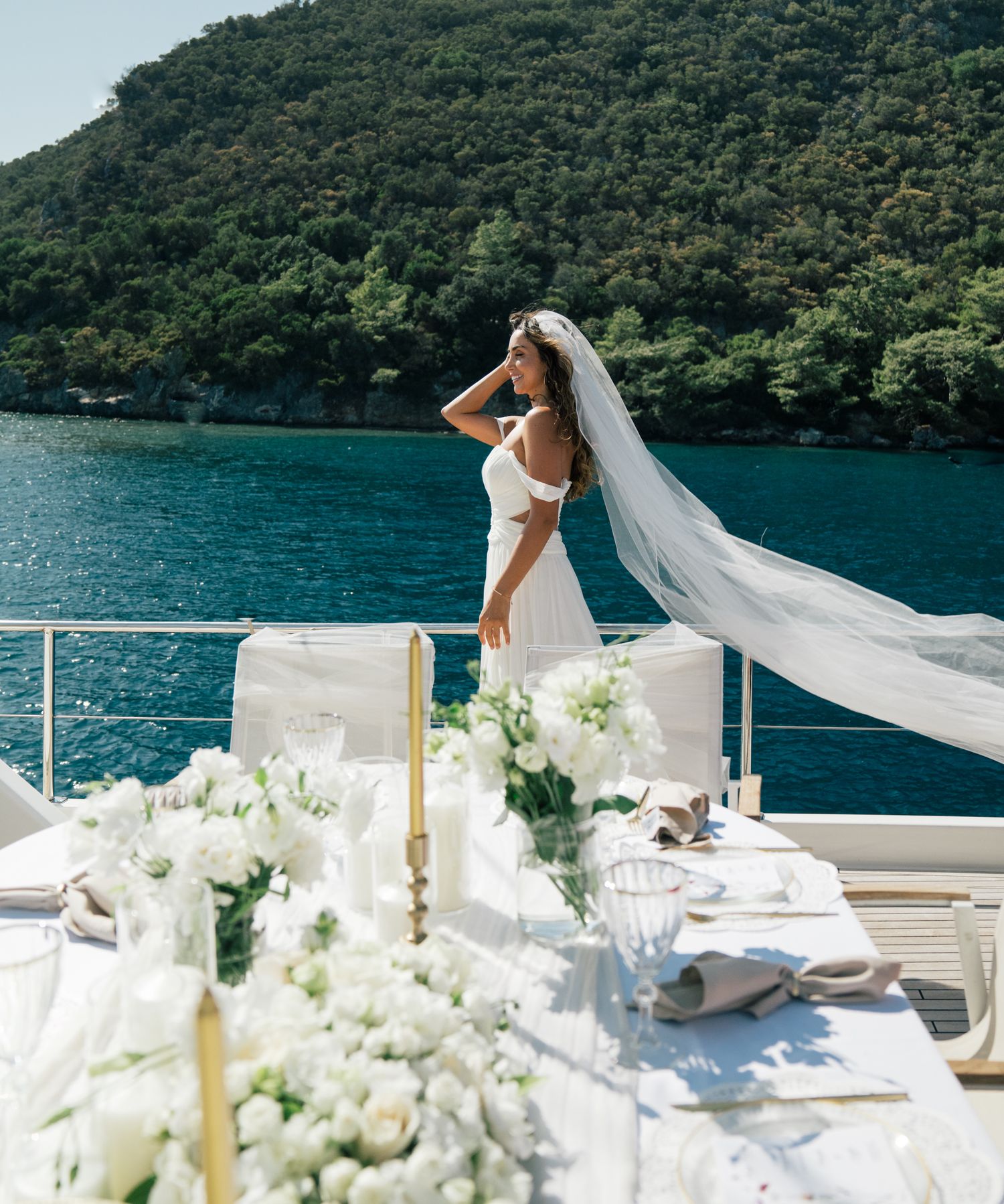 A wedding reception setup on a luxury yacht with white floral arrangements and a scenic mountain lake backdrop.