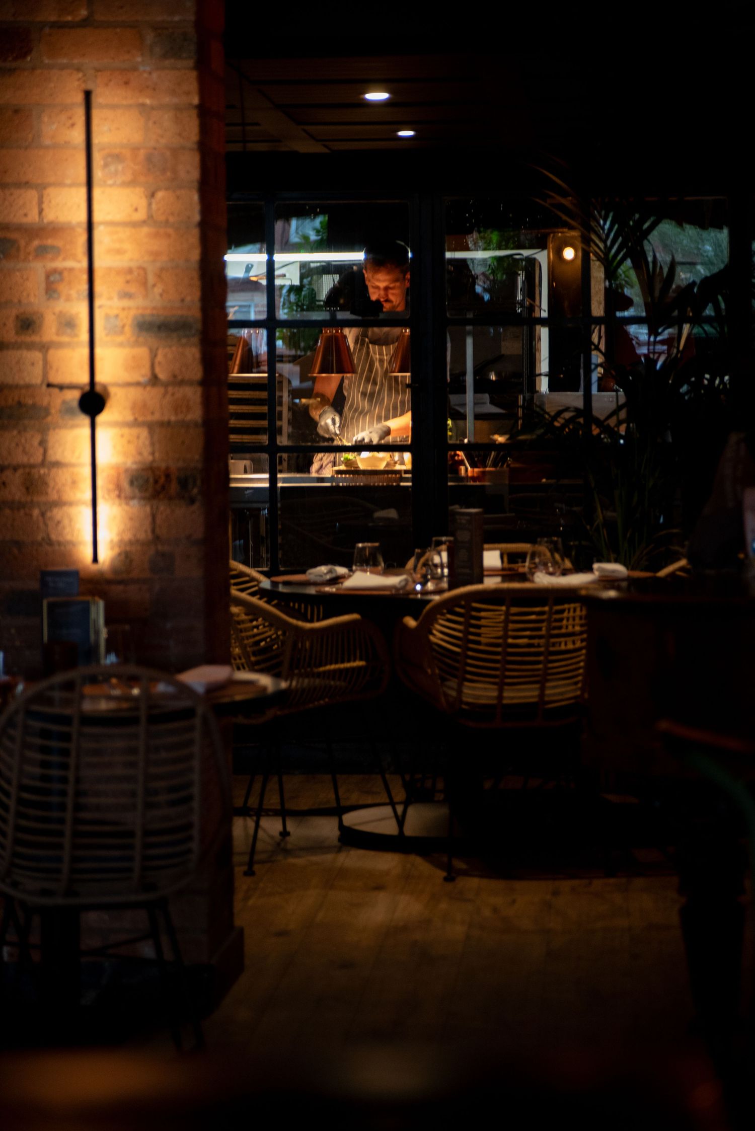 Chef plating dish in open kitchen, moody restaurant interior, professional food and hospitality photography showcasing dining atmosphere
