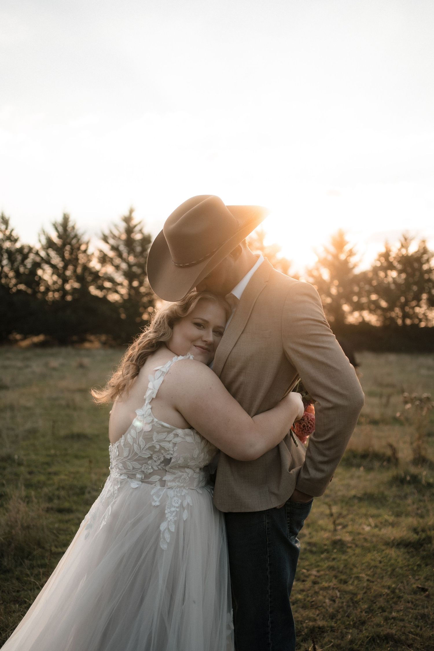 Romantic sunset wedding portraits show tender moments between newlyweds in a golden field with evergreen trees.