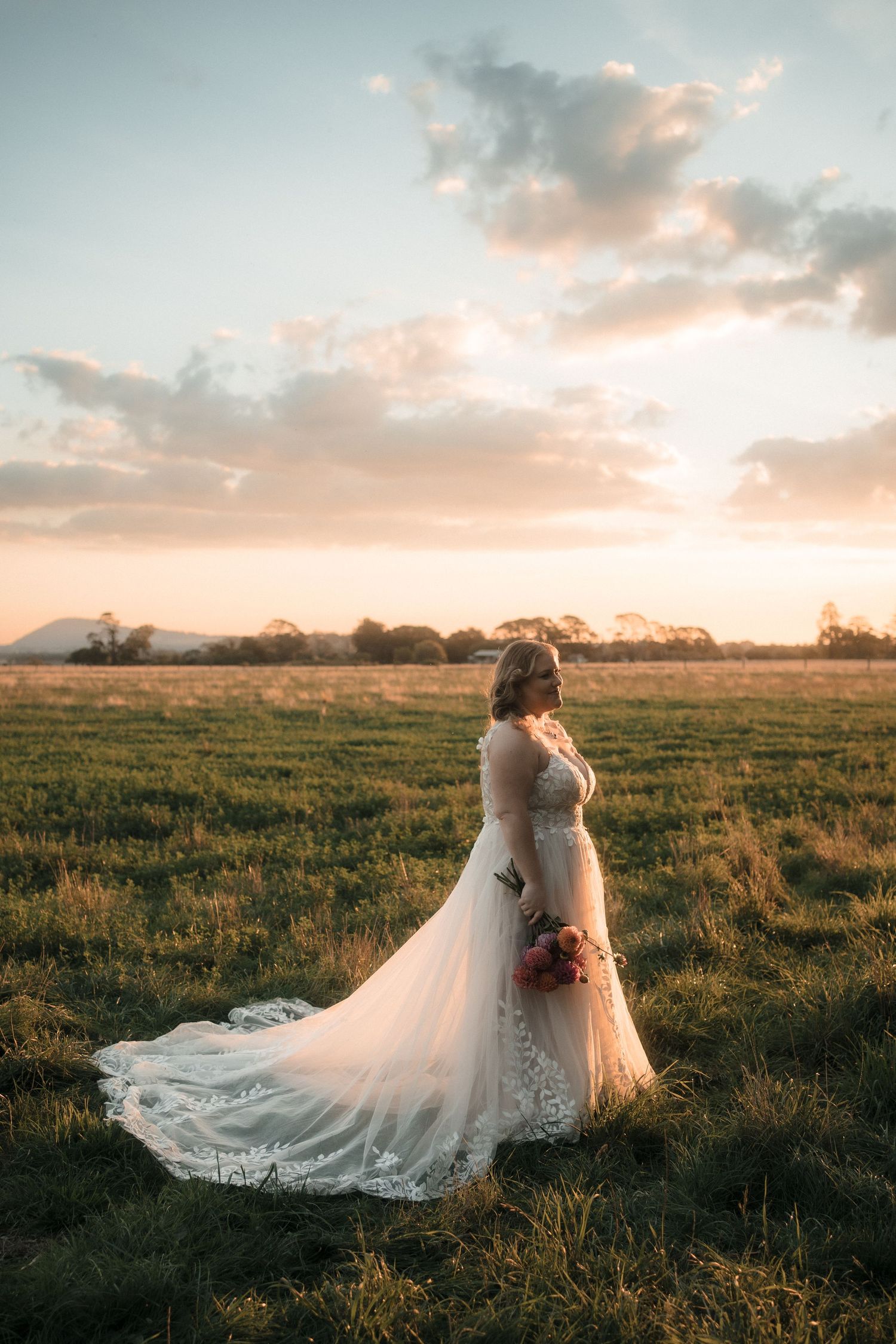 A romantic sunset wedding photo showing a flowing white dress trailing across a green meadow at golden hour.